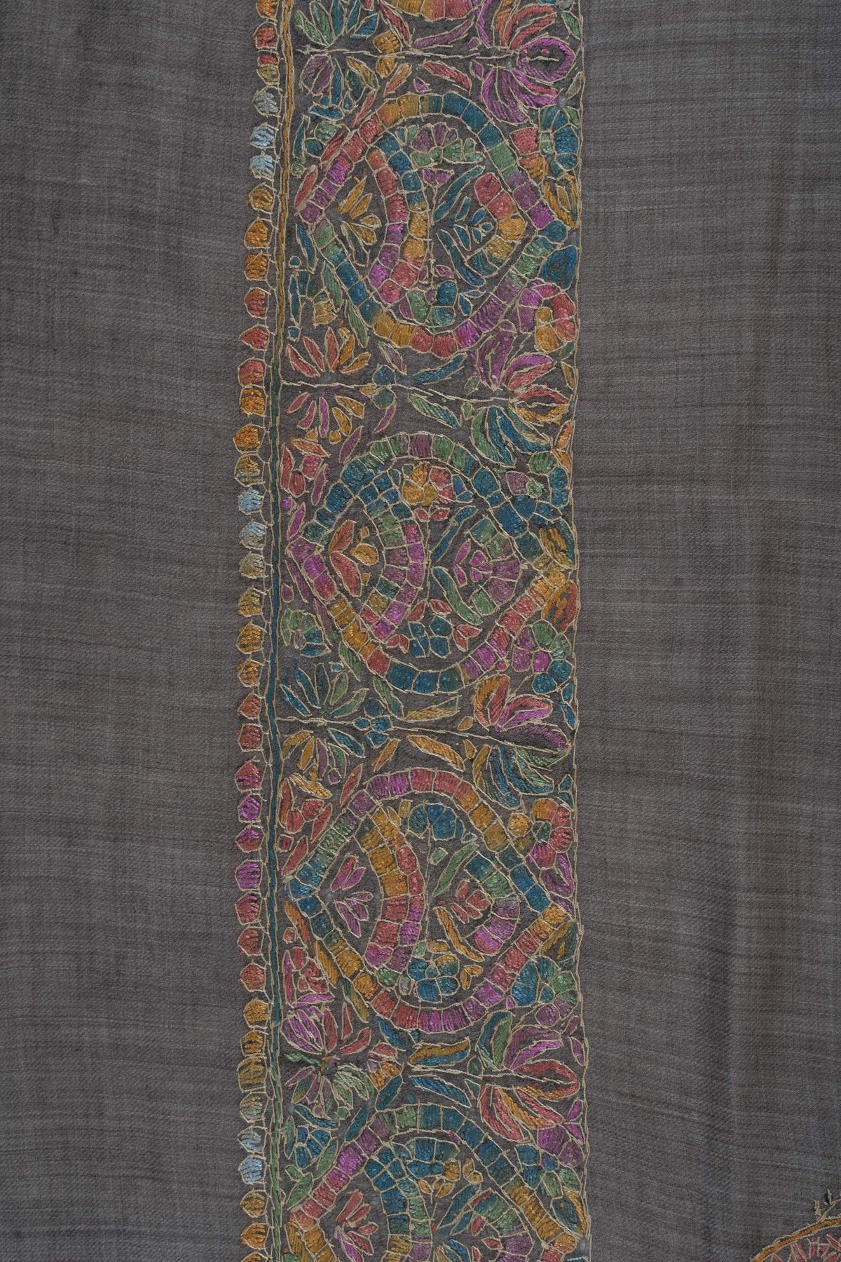 Close-up of Sozni border medallions in rose, teal, saffron and gold with fine lattice details on charcoal Merino wool.