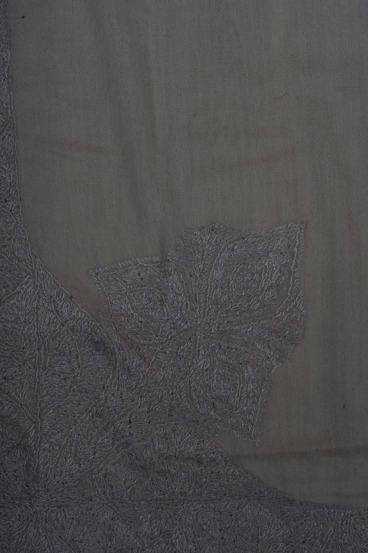 Close-up of a large silver-grey Sozni corner motif with pointed leaves and dense floral stitching on ivory Merino wool.