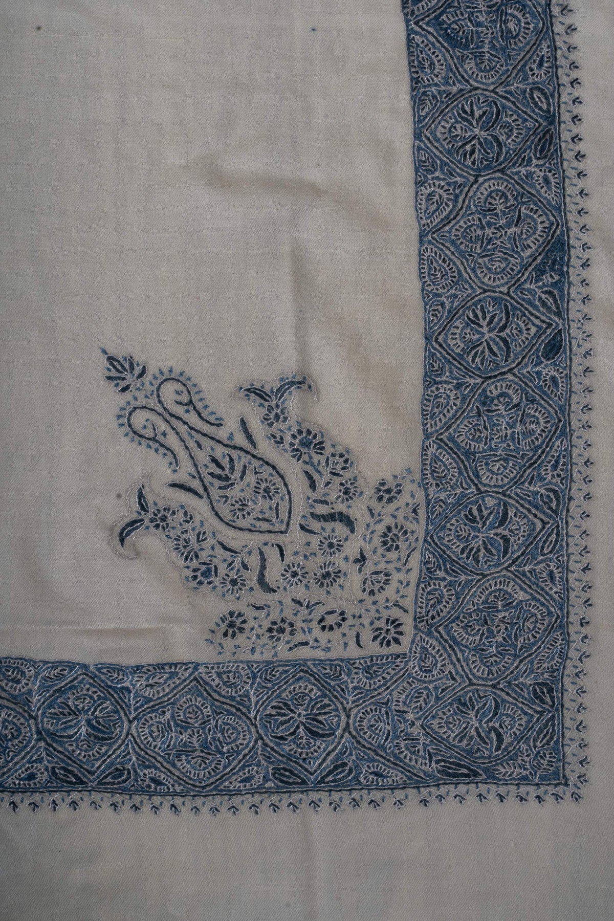 Ivory rumal corner showing an indigo paisley crest beside the dense embroidered border.