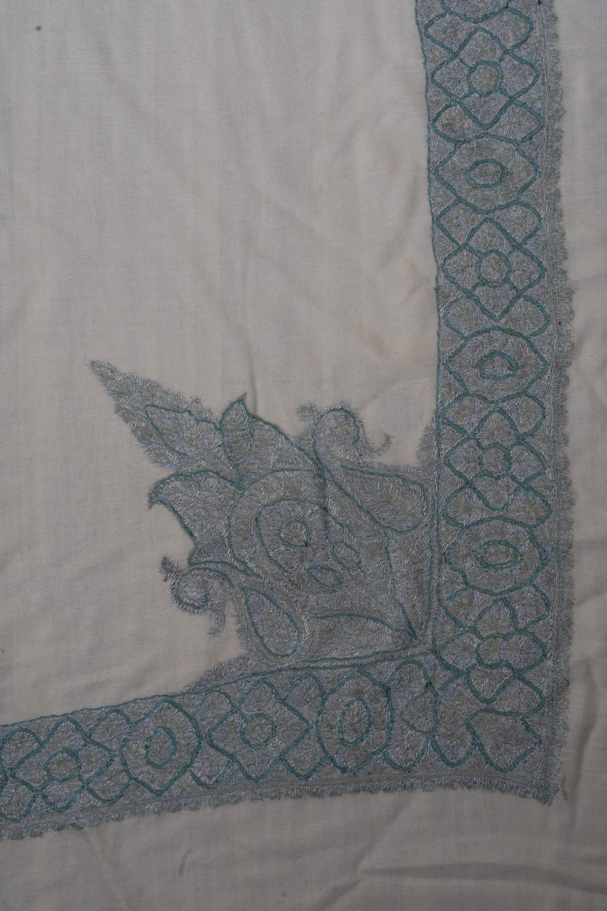 Ivory rumal corner showing a large pointed floral motif joining the icy-blue embroidered border.