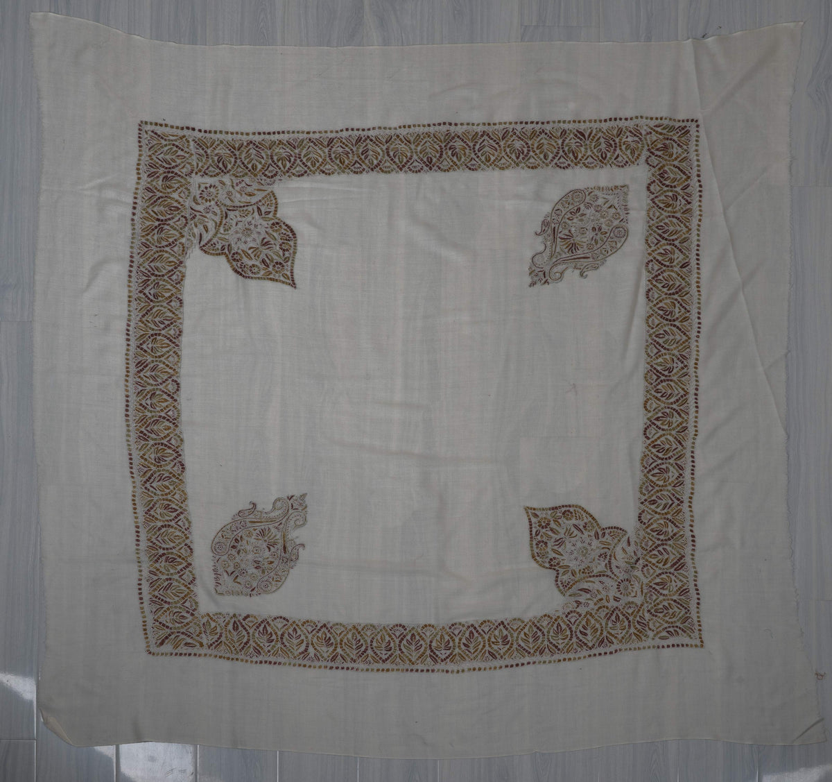 Ivory square Merino wool rumal laid flat with amber, olive and rust Sozni borders, two separate motifs and two large leafy corners.
