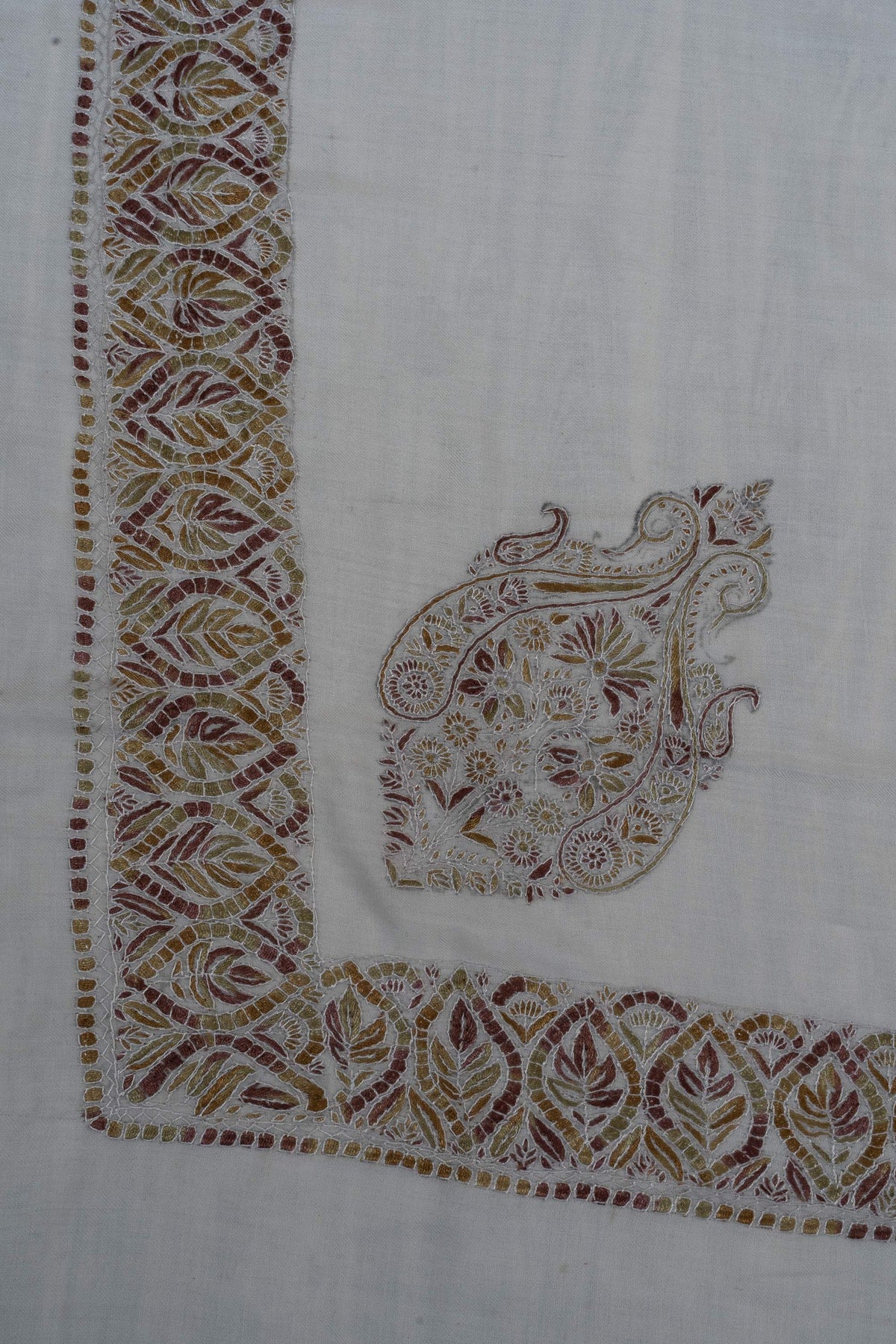 Corner of an ivory Merino wool rumal with an ornate Sozni floral motif and amber, olive and rust leaf borders.