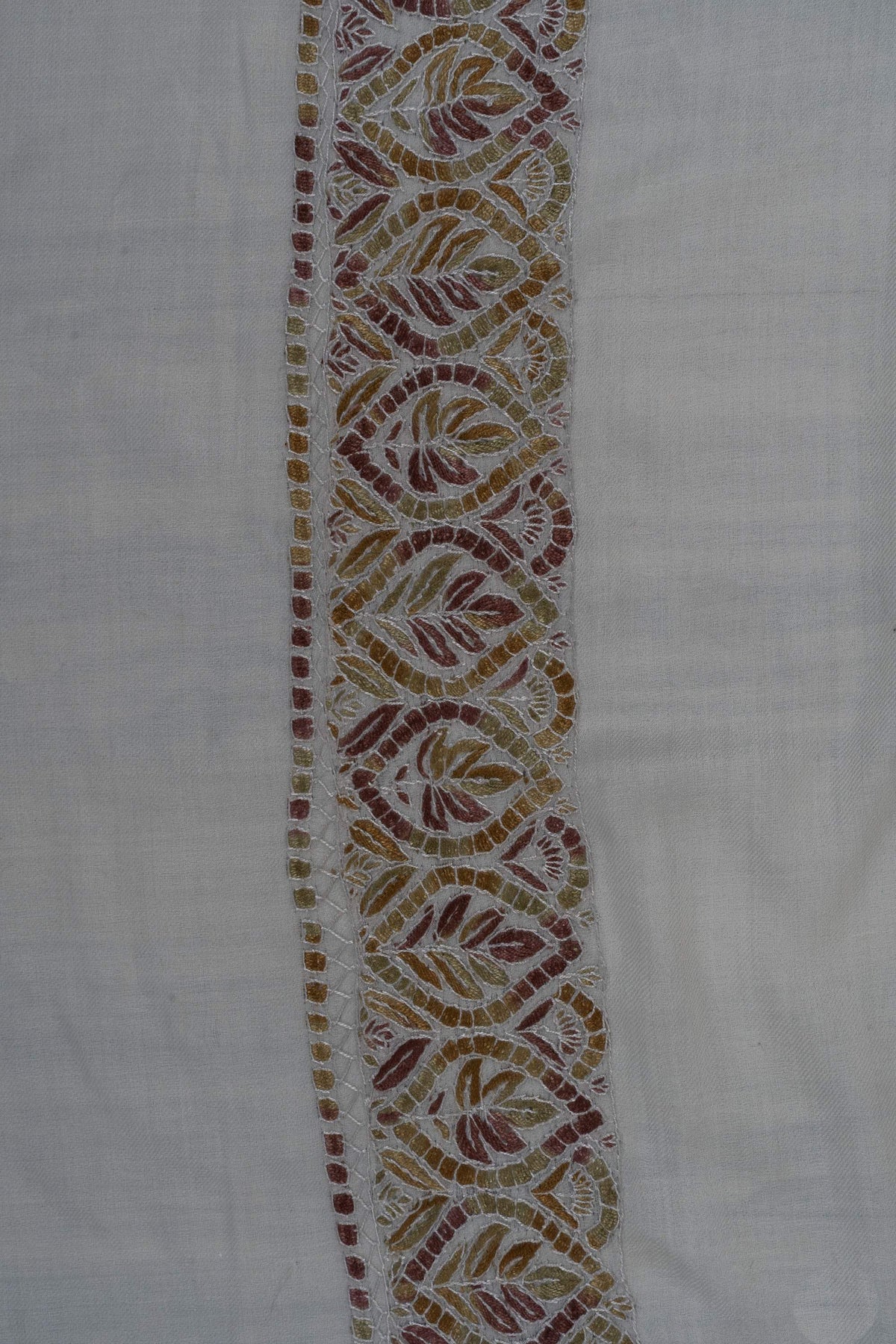 Close-up of repeating Sozni leaf motifs in amber, olive and rust with pale stitching on an ivory Merino wool border.