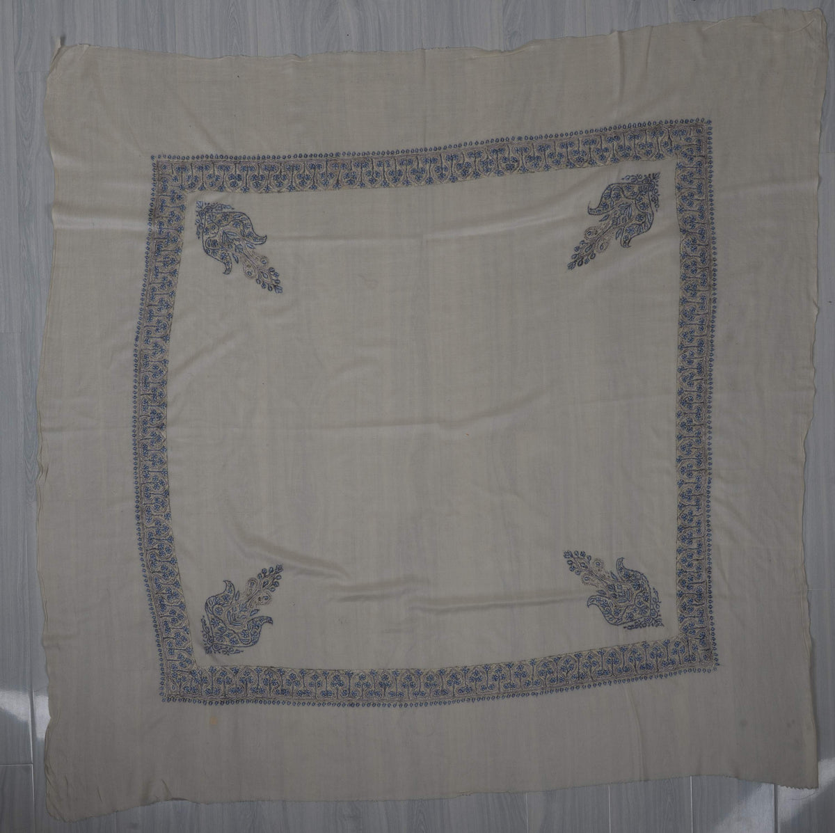 Ivory square Merino wool rumal laid flat with blue Sozni floral borders, four corner paisleys and a plain centre.