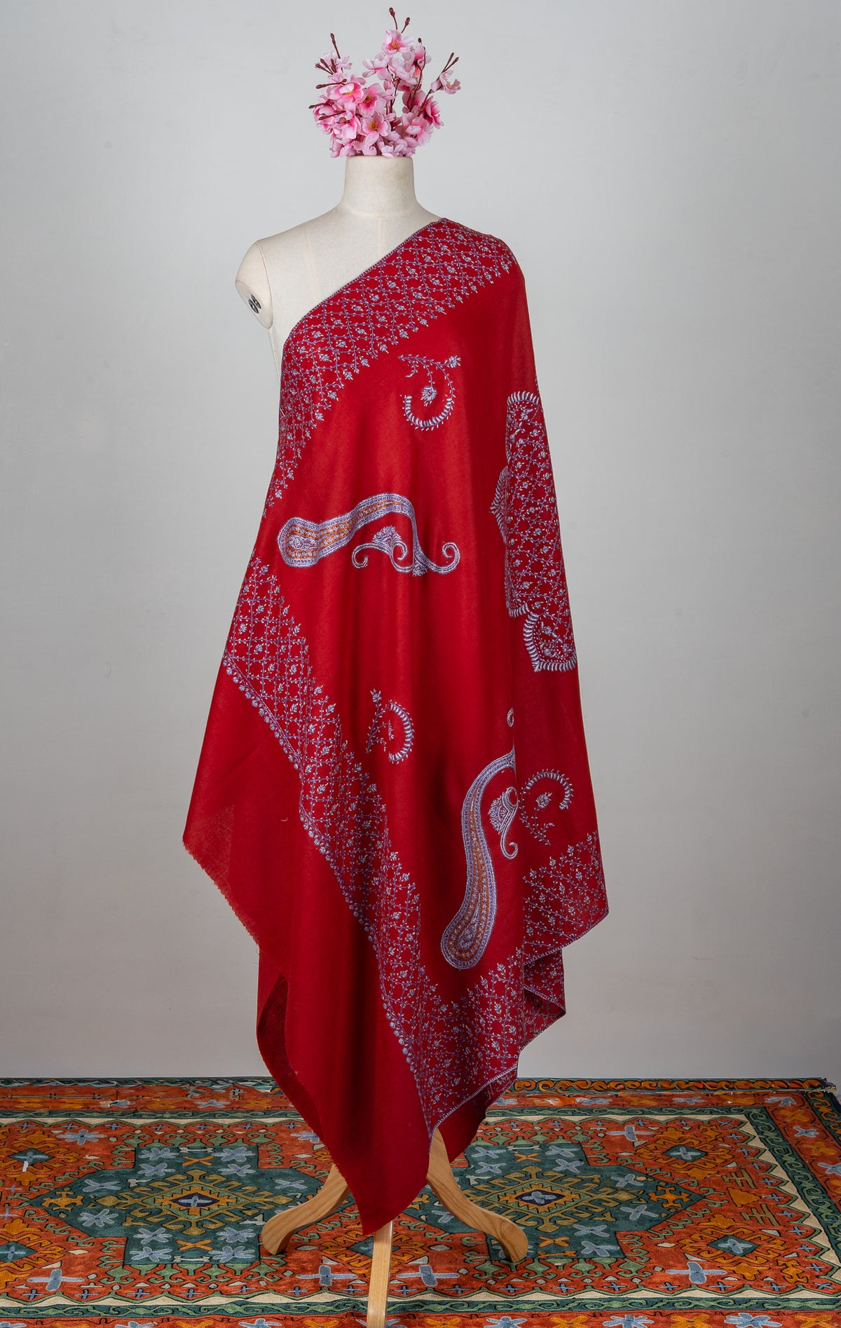 Ruby-red Merino wool shawl draped on a mannequin, with pale Sozni paisleys and densely embroidered floral borders