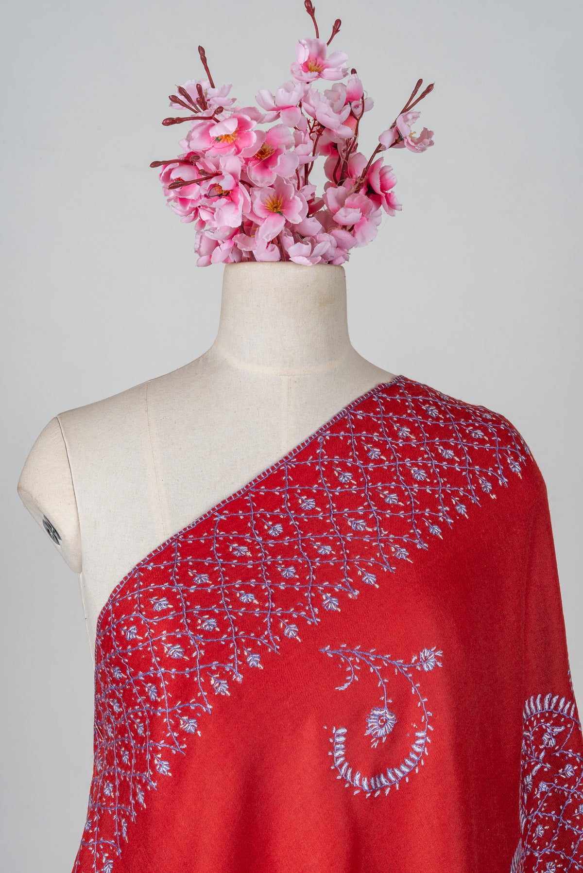 Ruby-red Merino wool shawl draped across a mannequin shoulder with pale lavender Sozni floral latticework and a curved sprig