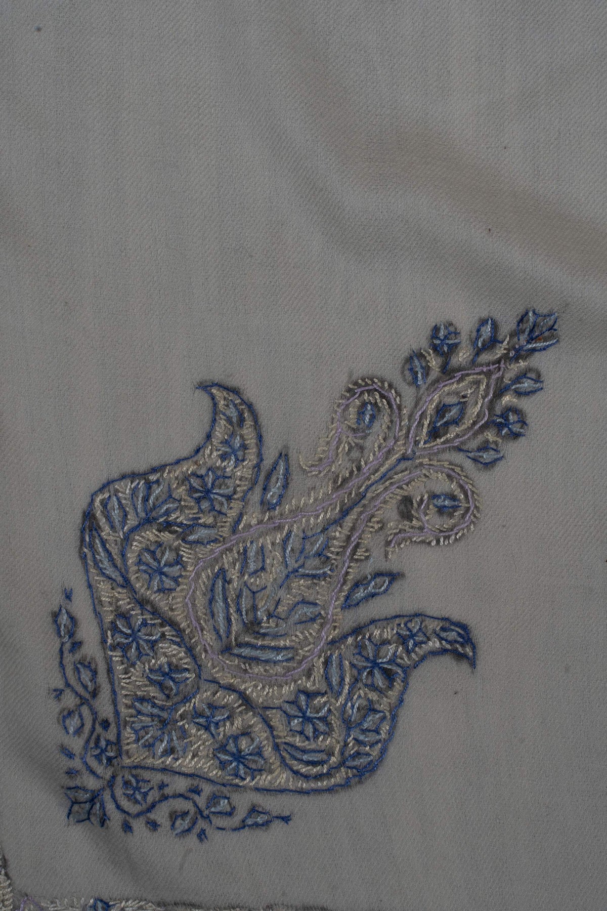 Close-up of a blue Sozni paisley filled with fine flowers, leaves and pale stitching on ivory Merino wool.