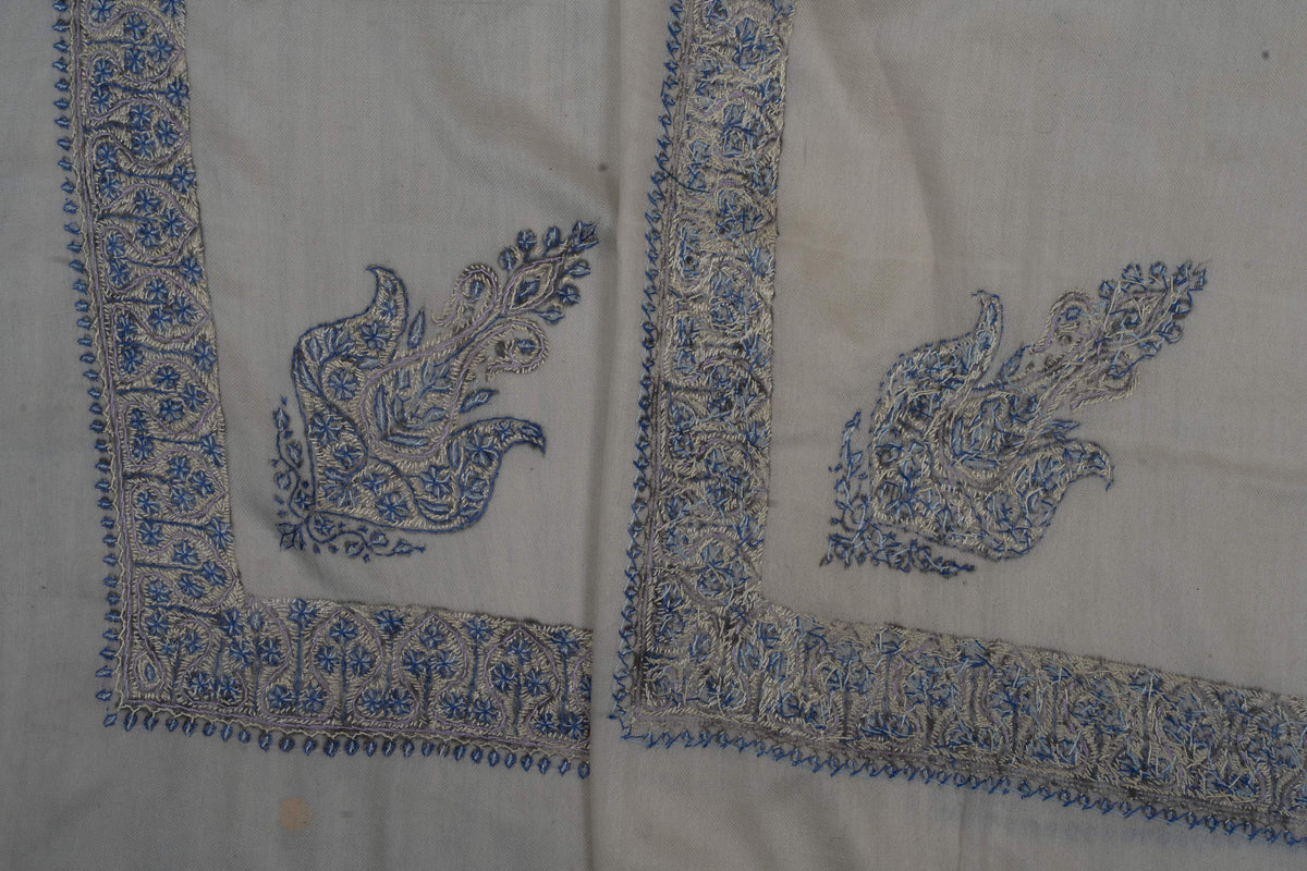 Two ivory Merino wool rumal corners showing blue paisleys and the front and reverse of Sozni floral border stitching.