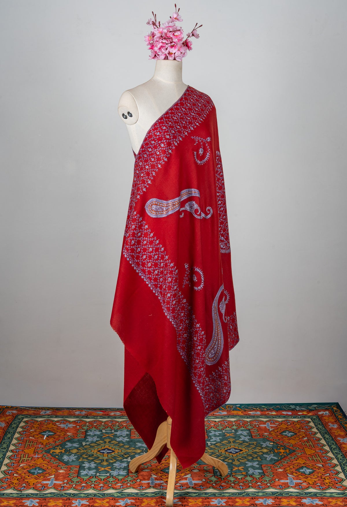 Full view of a ruby-red Merino wool shawl on a mannequin with large pale paisleys and floral Sozni borders