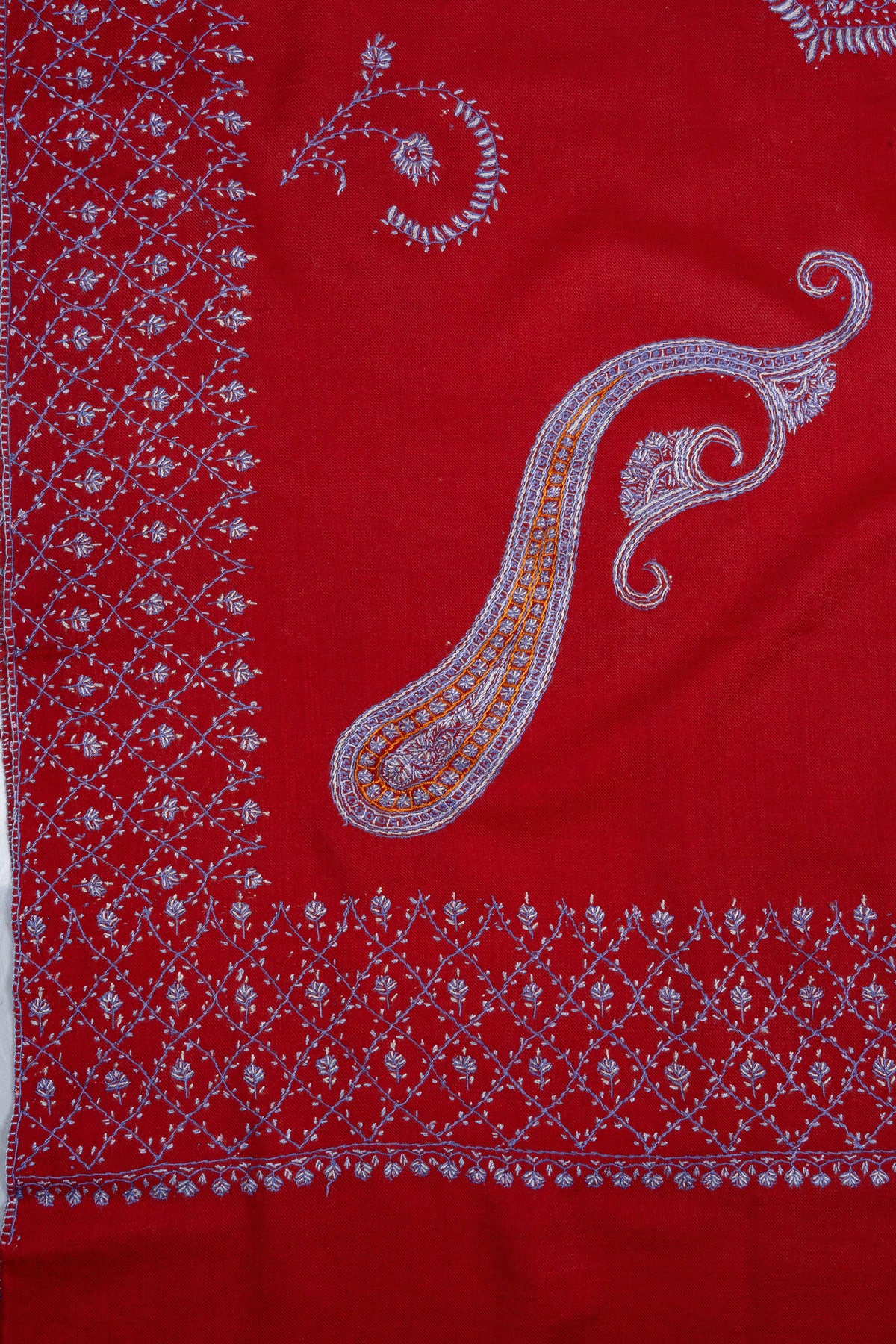Corner detail of a ruby-red shawl with a sweeping lavender and gold-toned paisley inside floral Sozni borders