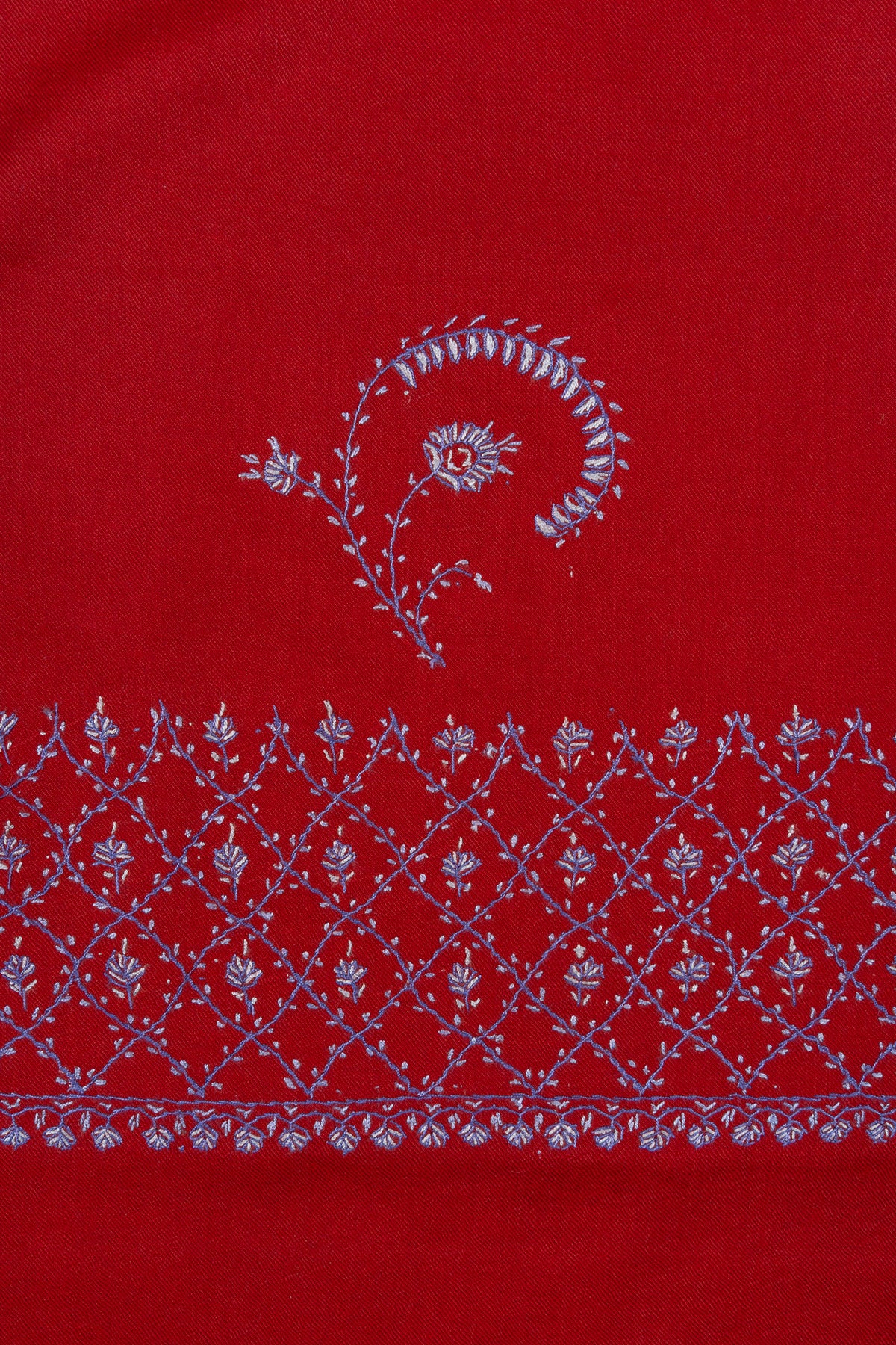 Close-up of a curved pale Sozni floral sprig above a latticework border on ruby-red Merino wool