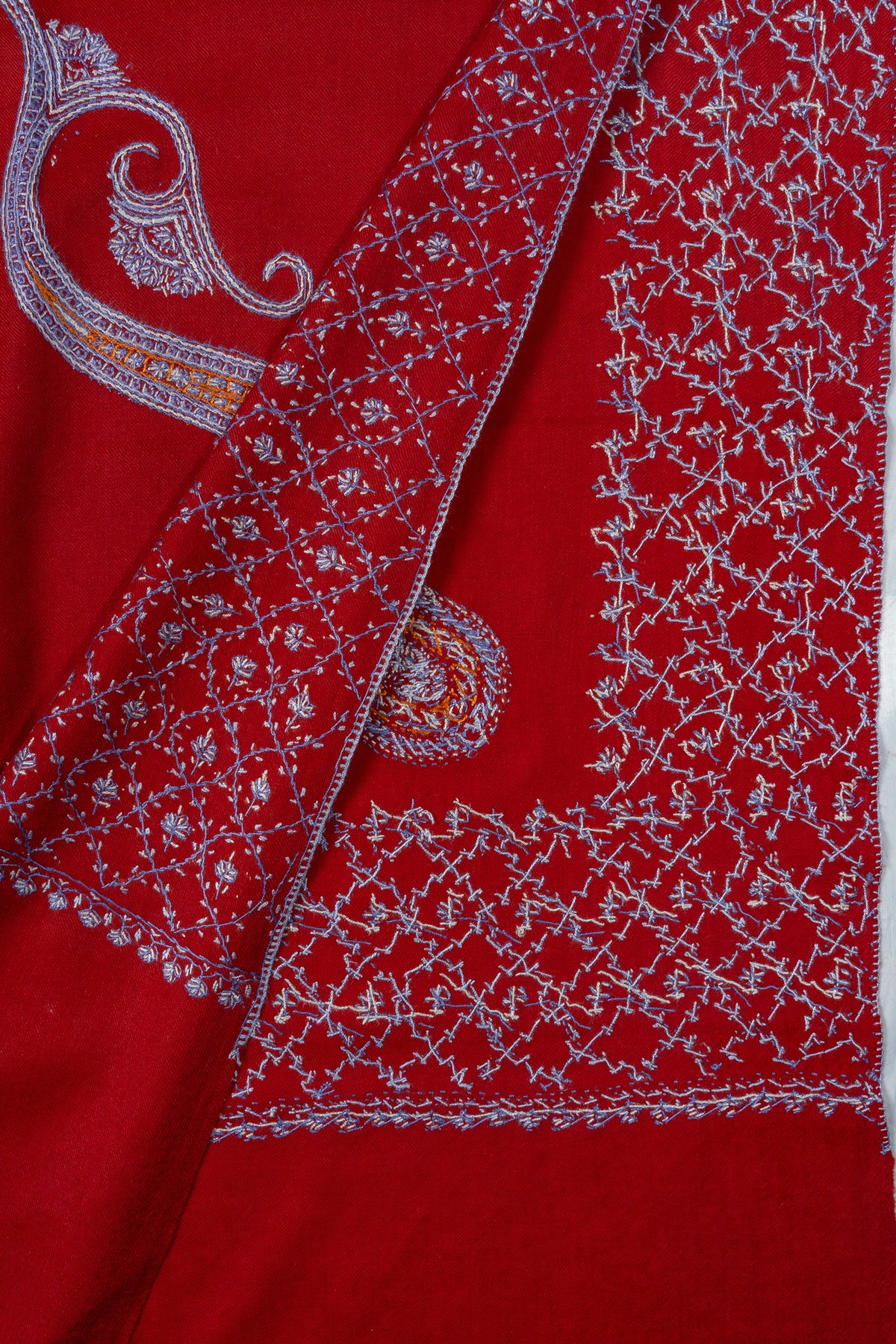 Overlapping corners of a ruby-red shawl showing pale Sozni paisleys and floral lattice stitching on both sides
