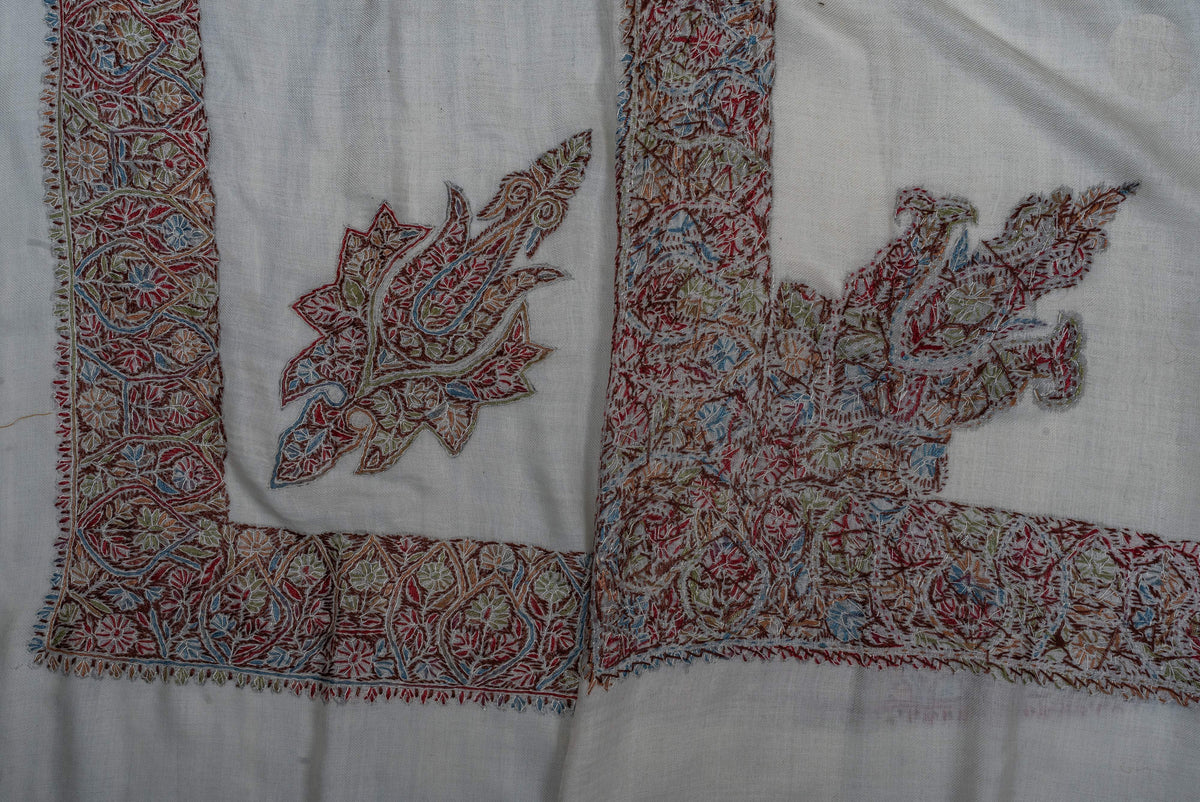 Folded ivory rumal corners showing both sides of the muted red, green, blue and ochre embroidery.