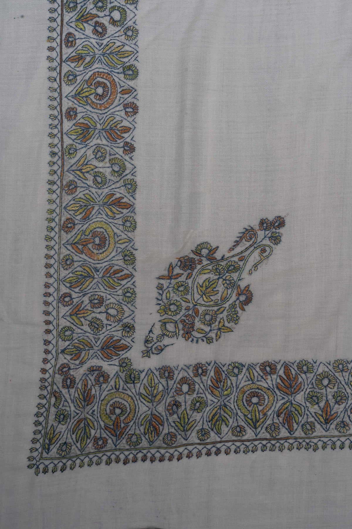 Corner of a pale Merino wool rumal with a sage, blue and ochre Sozni paisley and matching floral borders.