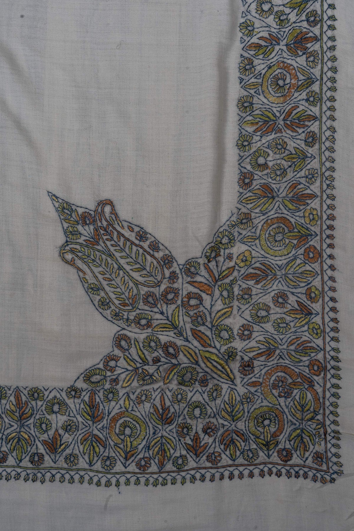 Large Sozni leaves and flowers rise from the border at one corner of a pale Merino wool rumal in sage, blue and ochre.