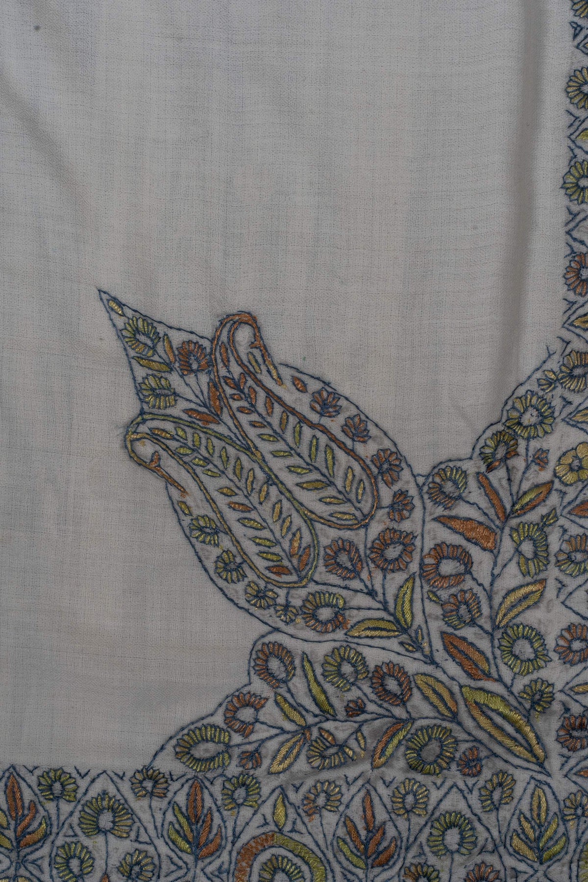 Close-up of a large Sozni corner motif with curled leaves, small flowers and blue outlines on pale Merino wool.
