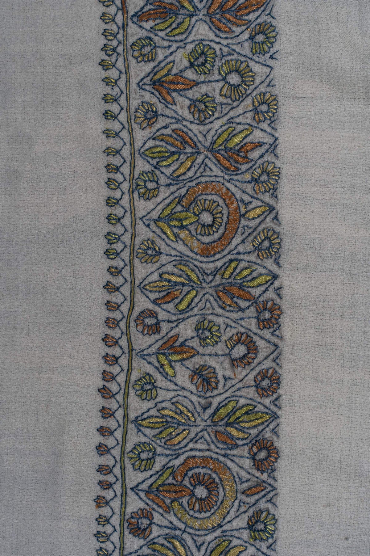 Close-up of sage, blue and ochre Sozni flowers and leaves arranged in repeating border panels on pale Merino wool.