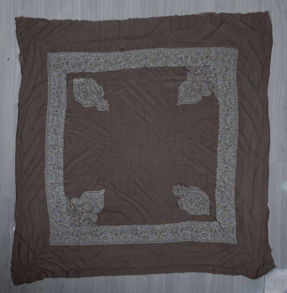 Square taupe rumal laid flat with pale blue-grey Sozni borders, two connected corner panels, two separate crests and a plain centre