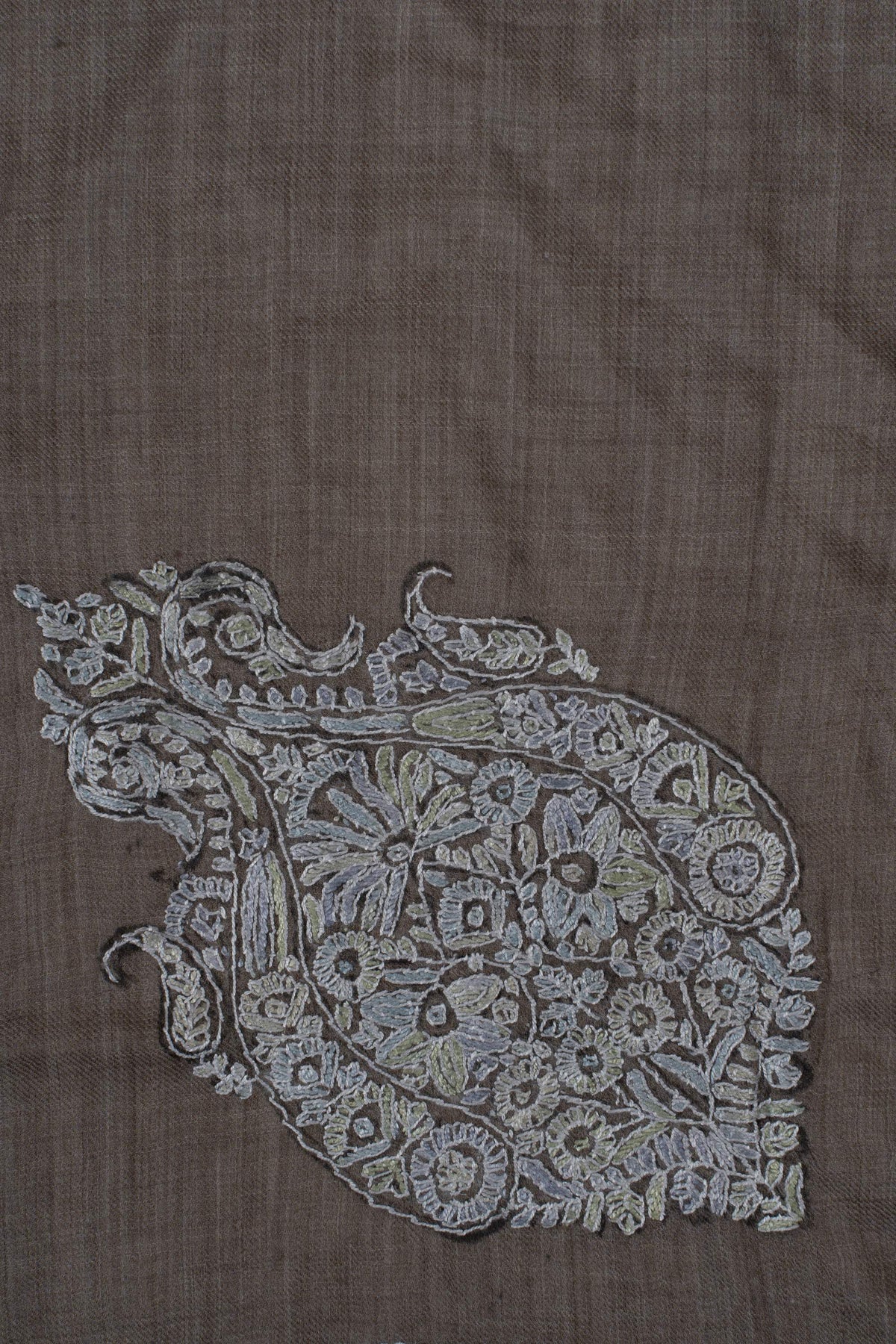 Close-up of a pale blue-grey Sozni floral crest filled with small flowers and curling leaves on taupe fabric