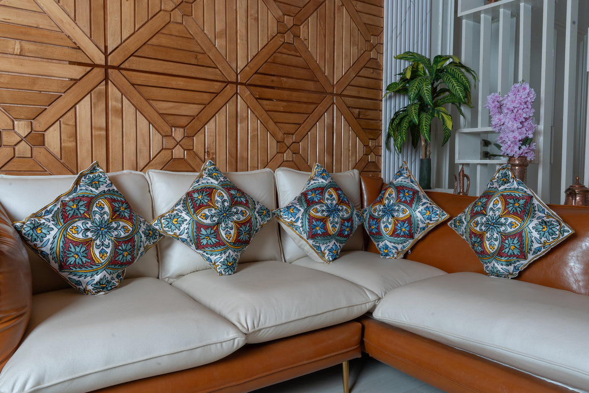 Five matching teal, burgundy and ivory embroidered cushions arranged across a cream corner sofa beneath wooden wall panels