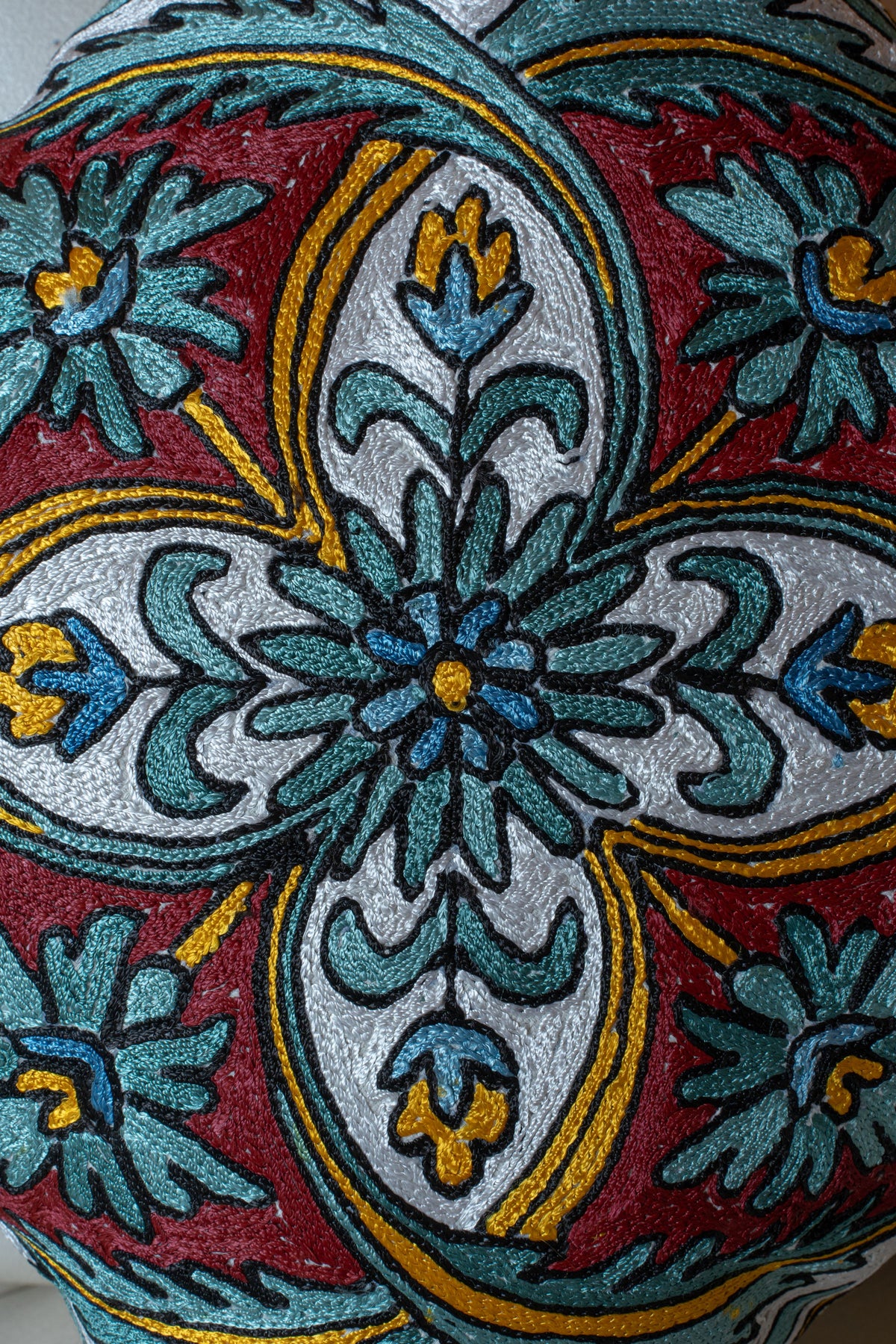 Close-up of a cushion’s teal and blue floral medallion, ivory curved panels, burgundy background and yellow accents