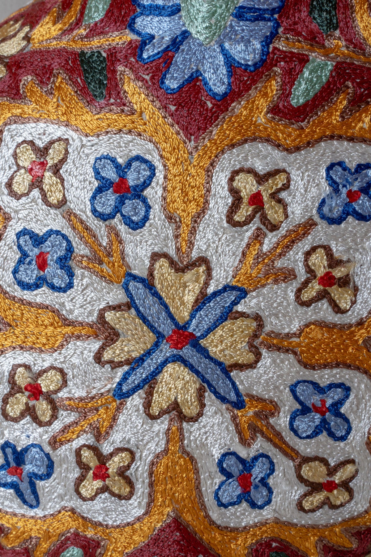 Close-up of blue, gold and rust floral embroidery with white-filled petals on a cotton cushion cover