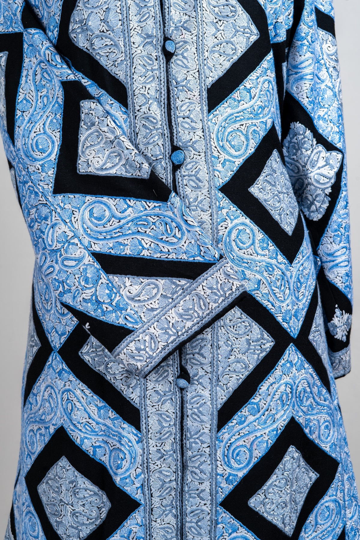 Close-up of the ice-blue jacket’s crossed cuff and button placket, with pale embroidered paisleys and black angular bands