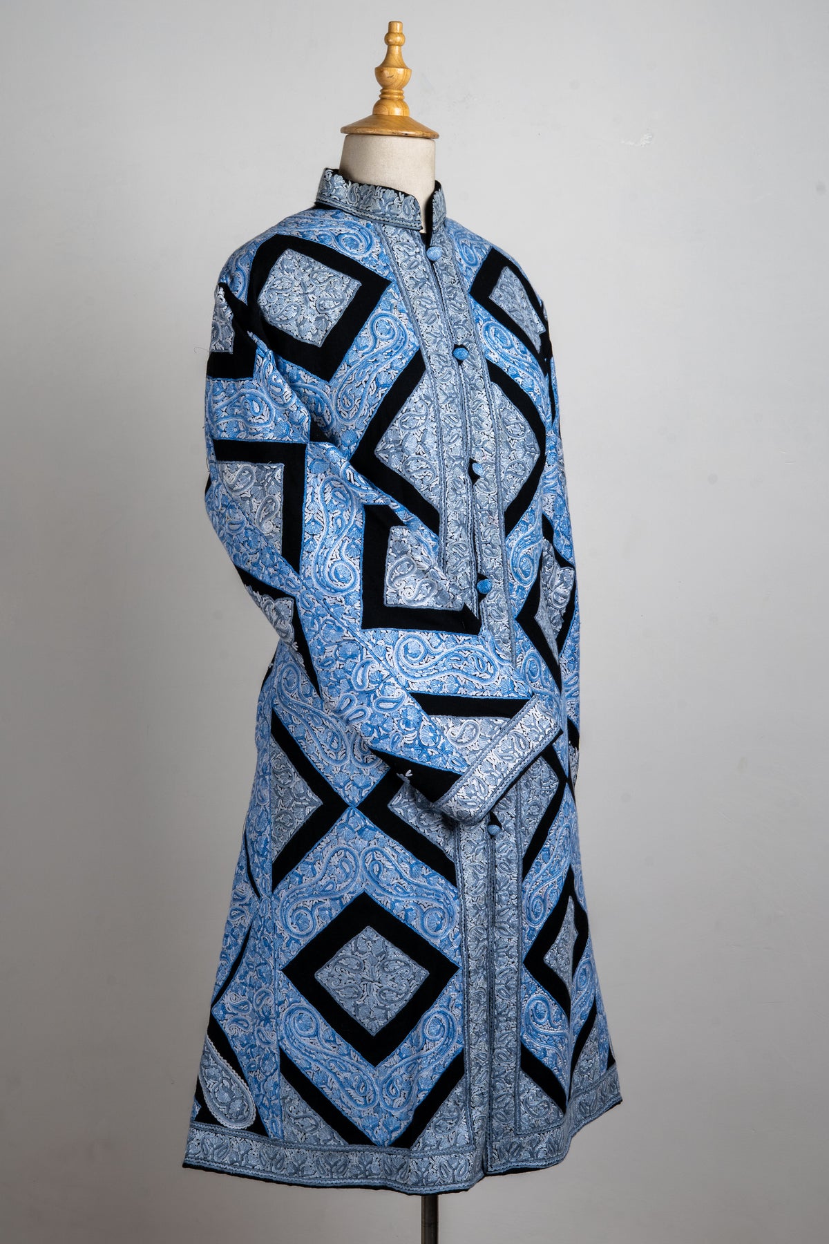 Angled full view of the ice-blue long jacket on a mannequin, with one sleeve crossed and bold black diamond outlines
