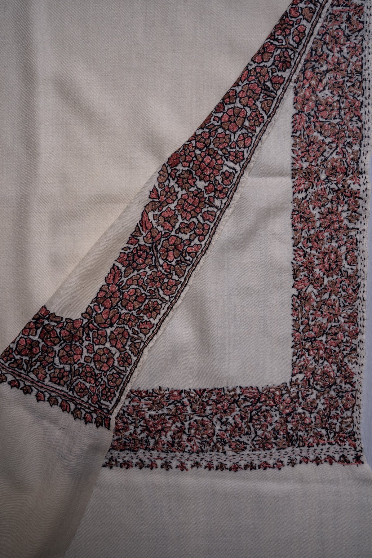 Overlapping corners of an ivory shawl showing both sides of red and black floral Sozni stitching