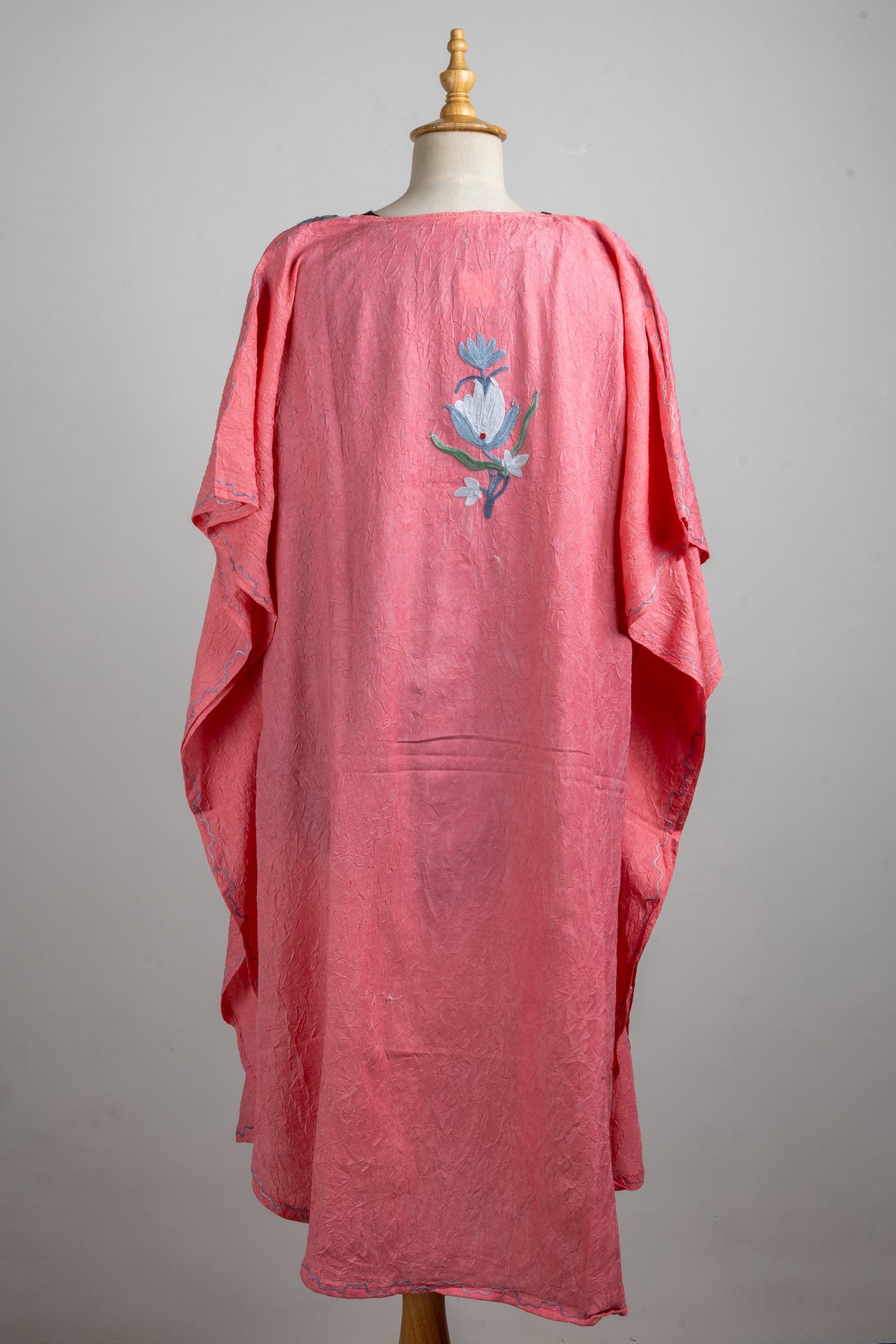 Back of the coral-pink kaftan, with a small blue-and-white floral motif between the shoulders and loose draped sleeves