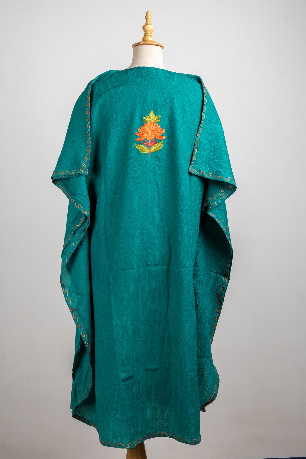 Back view of the teal kaftan with a small orange flower motif near the shoulders and delicate edging on the sleeves and hem.
