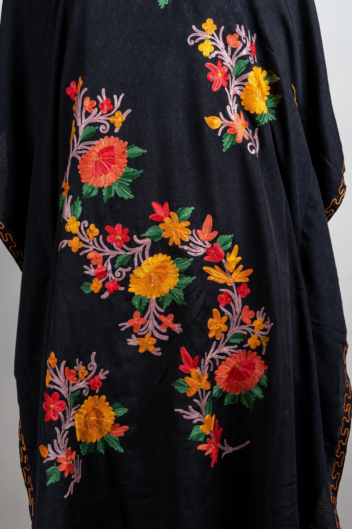 Close-up of red, orange and yellow Aari flower sprays with green leaves and pale pink curling stems on a black kaftan