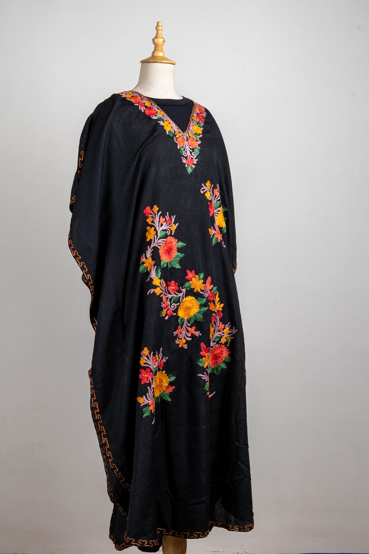 Angled full-length black kaftan on a mannequin with a floral V-neck, colourful Aari sprays and narrow golden edging