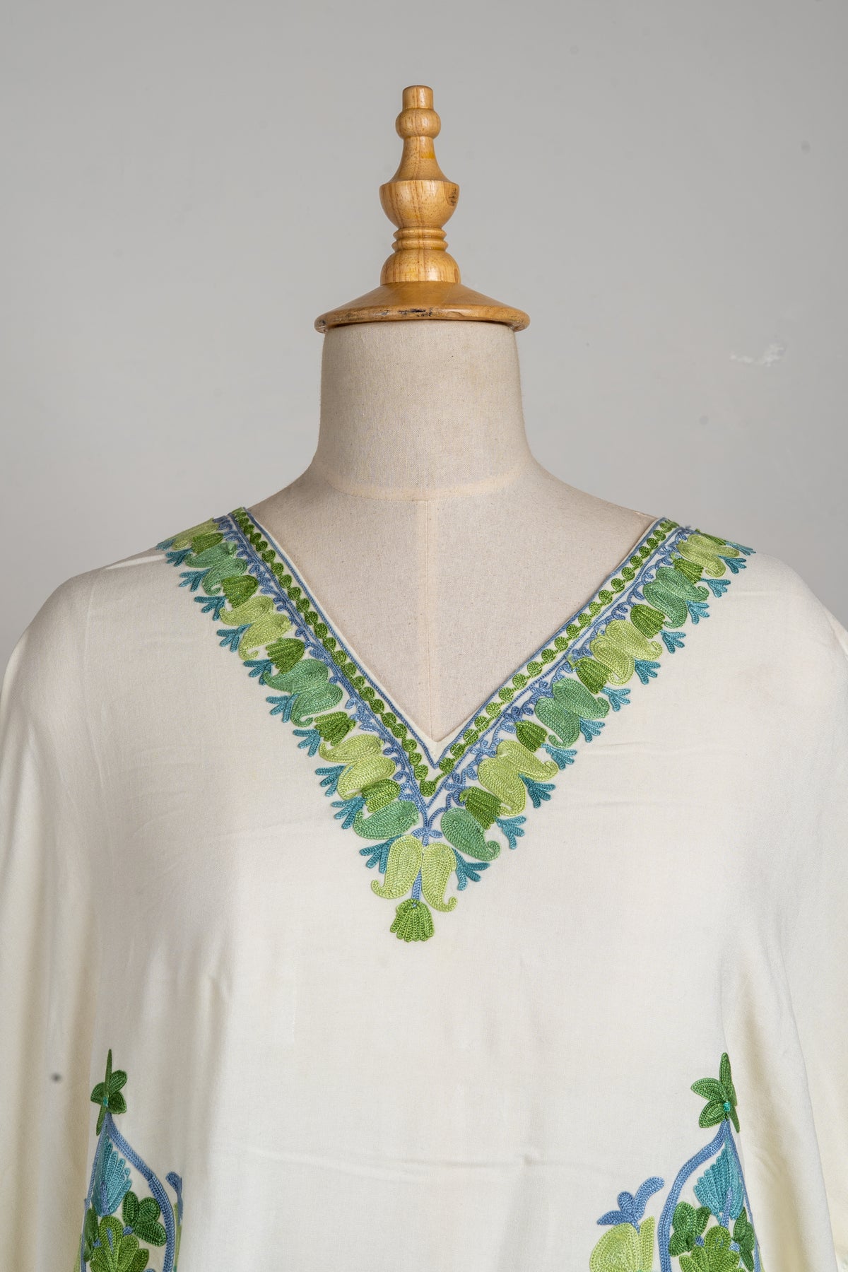 Close view of the ivory kaftan’s V-neck, edged with green and blue floral Aari embroidery