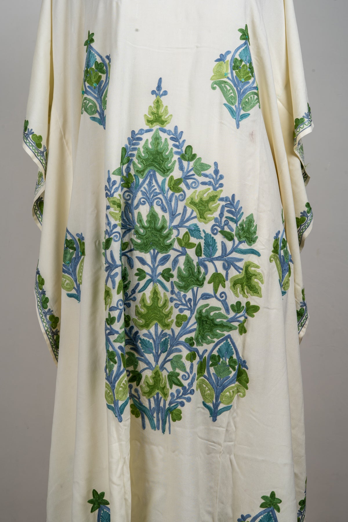 Close view of the large central green and blue floral bouquet on the ivory kaftan, surrounded by smaller motifs