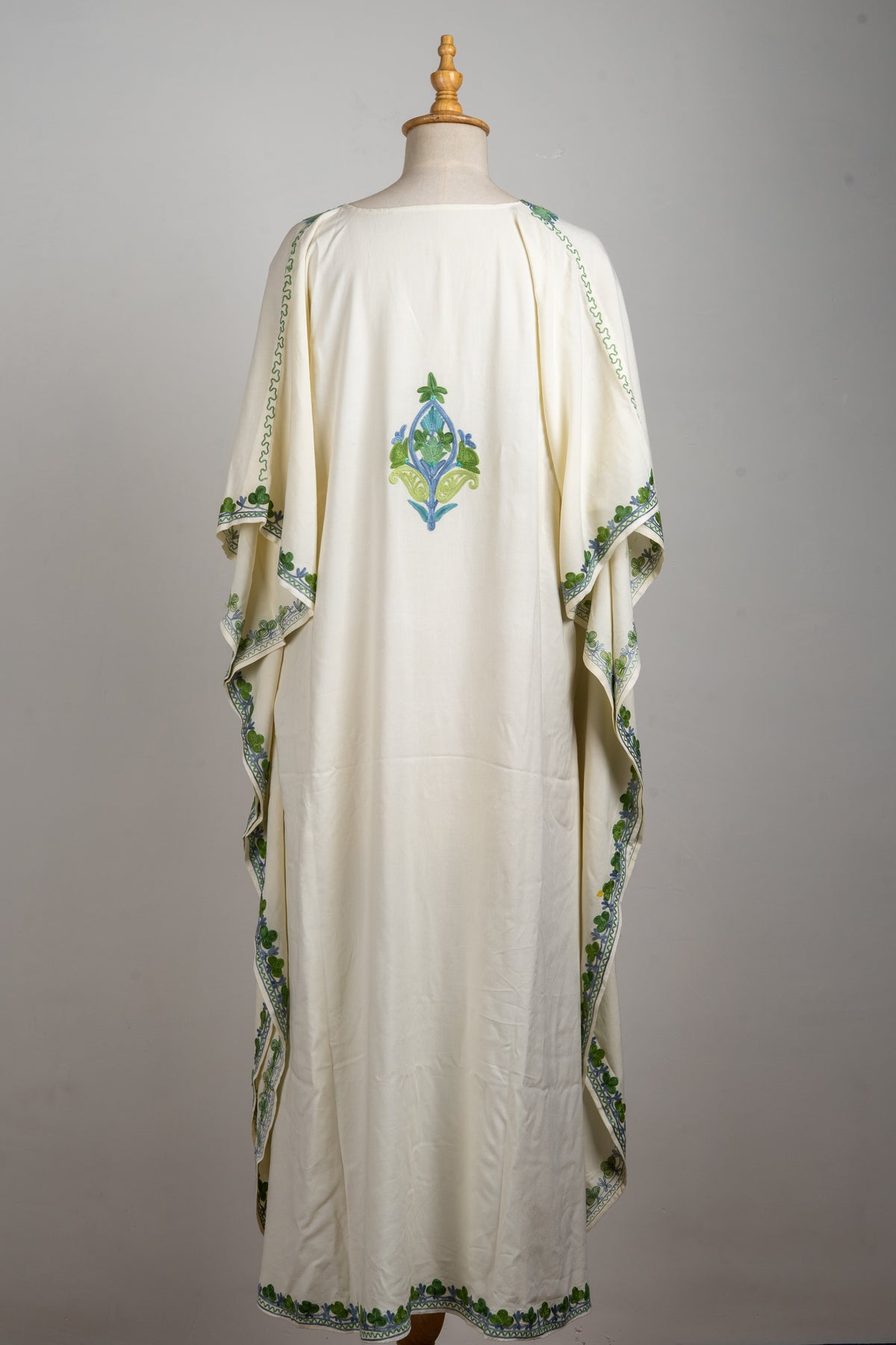 Back view of the ivory kaftan, with one green-blue floral motif and narrow embroidered sleeve and hem borders