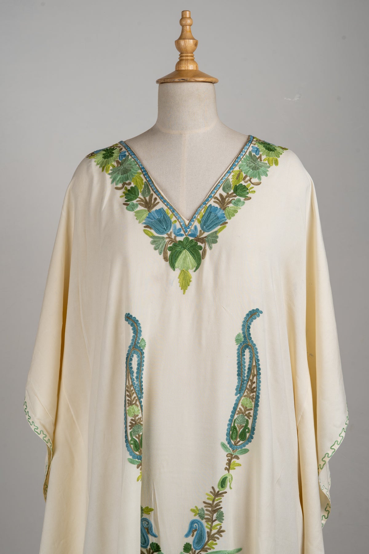 Upper front of an ivory kaftan with a blue-and-green embroidered V-neck and two long paisleys below
