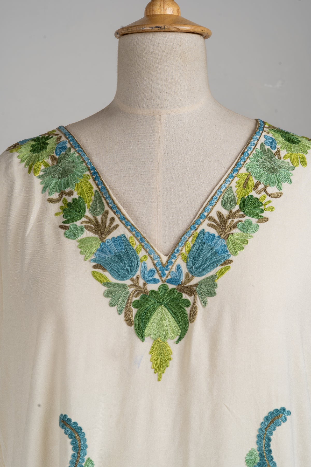 Neckline detail of the ivory kaftan, with blue flowers, green leaves and narrow blue-and-gold edging around the V-neck
