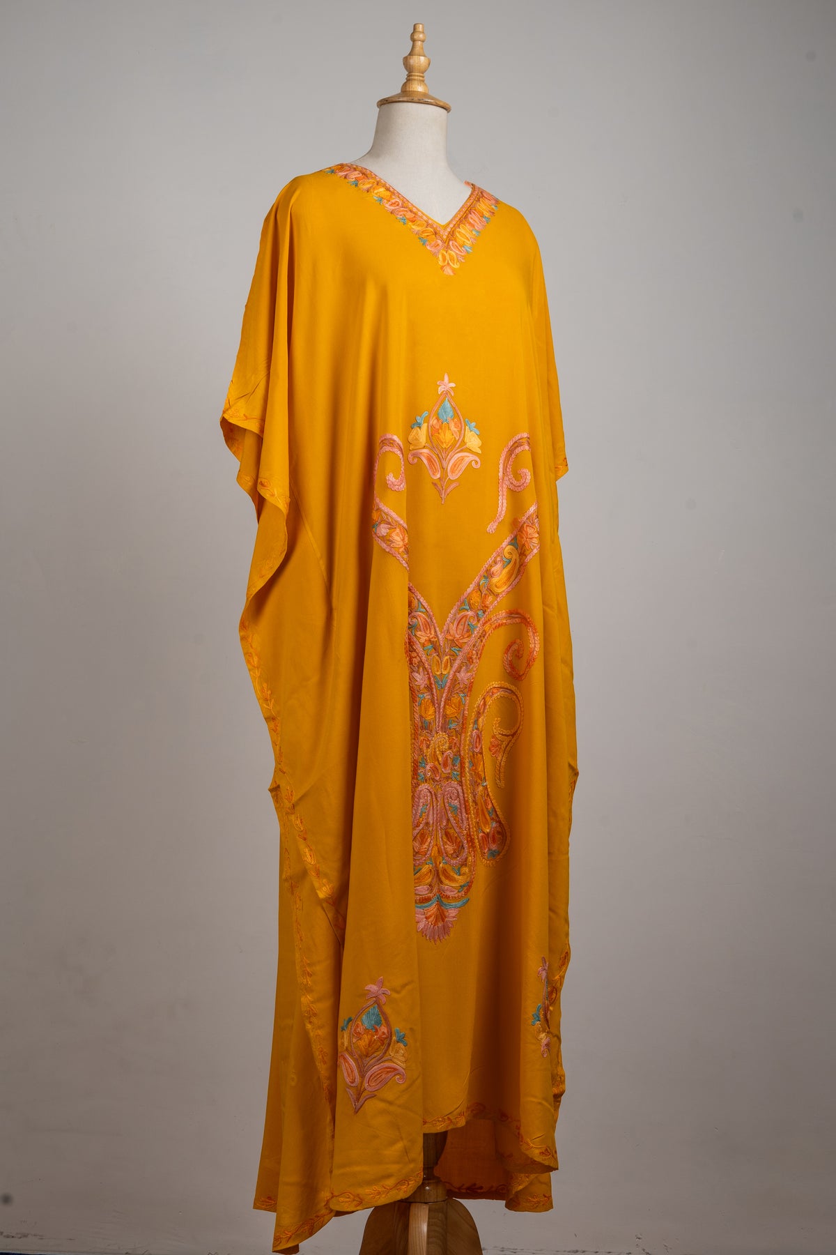 Full angled view of the golden-yellow kaftan, showing loose sleeves and long peach and blue paisley embroidery down the front.