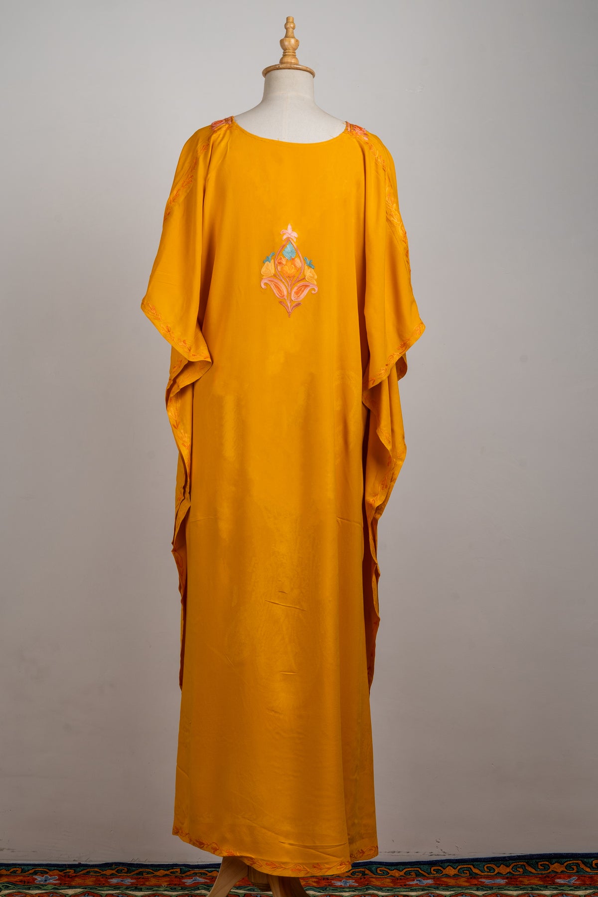 Back view of the golden-yellow kaftan with a small peach and blue motif between the shoulders and a long plain skirt.