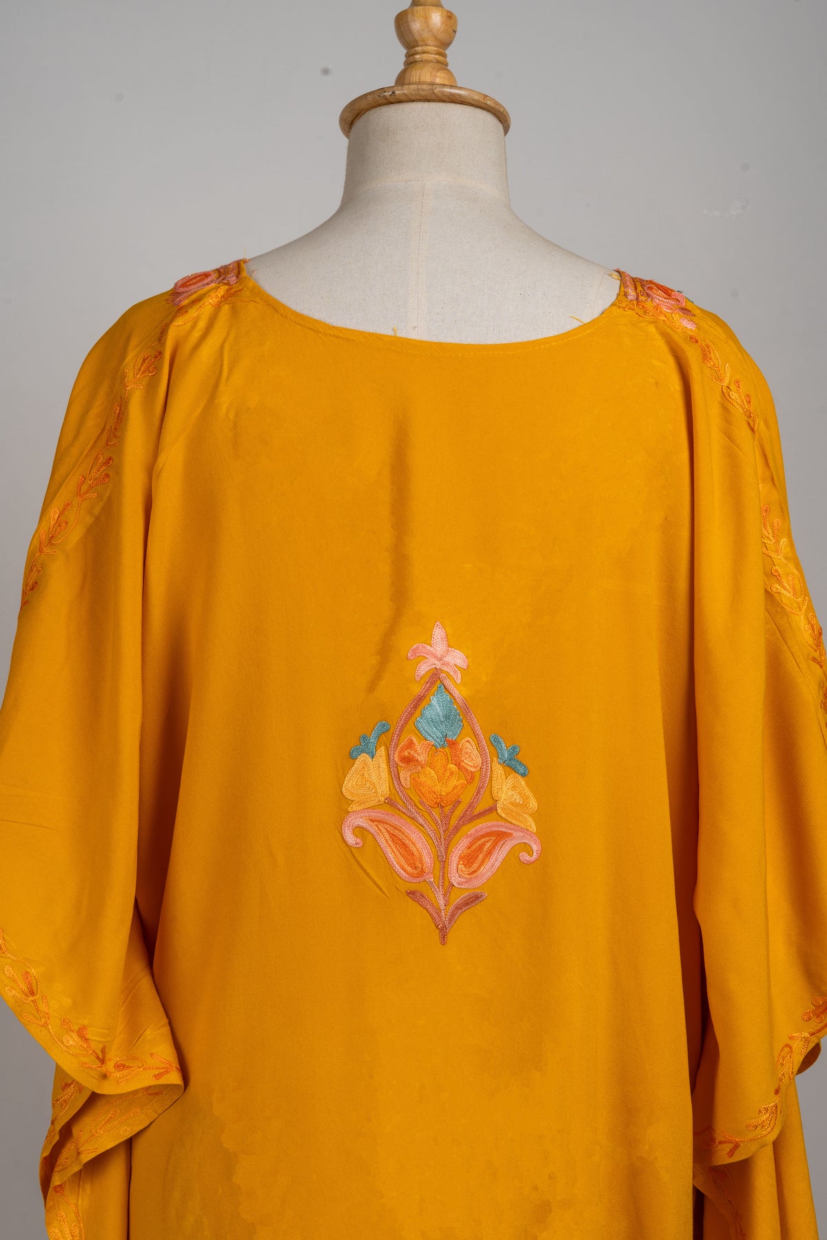 Upper back detail of the kaftan with a round neckline and a small peach, coral and pale blue embroidered motif.