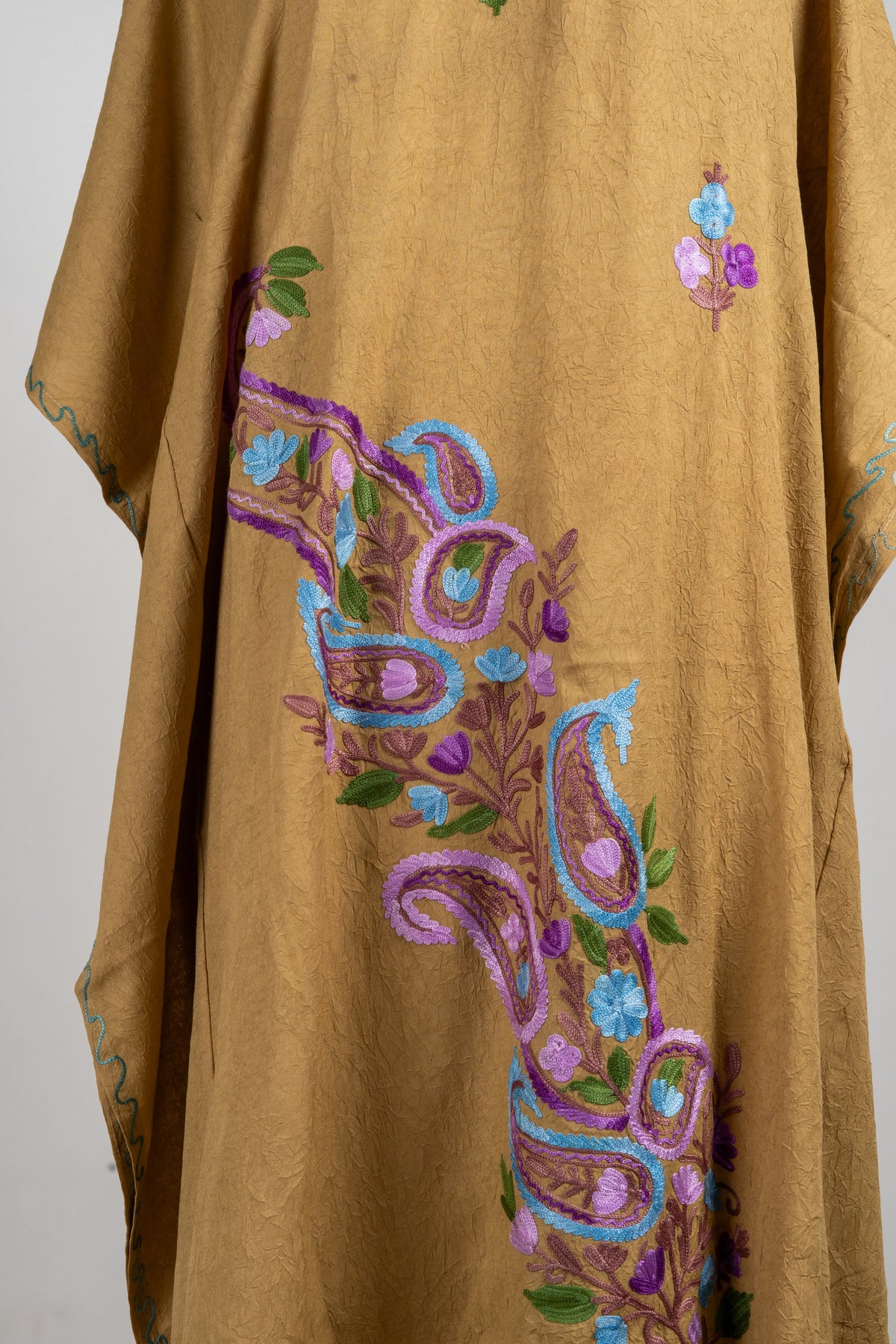 Close-up of the kaftan lower front with blue and lavender paisleys, small flowers and green leaves on camel fabric.