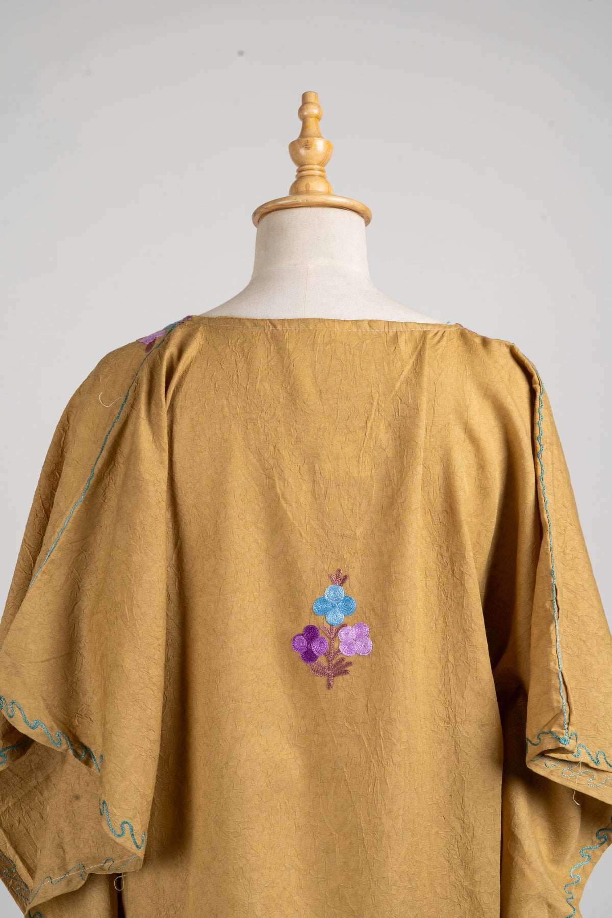 Upper back of the camel kaftan with a small blue and purple floral sprig and pale blue edging on the loose sleeves.