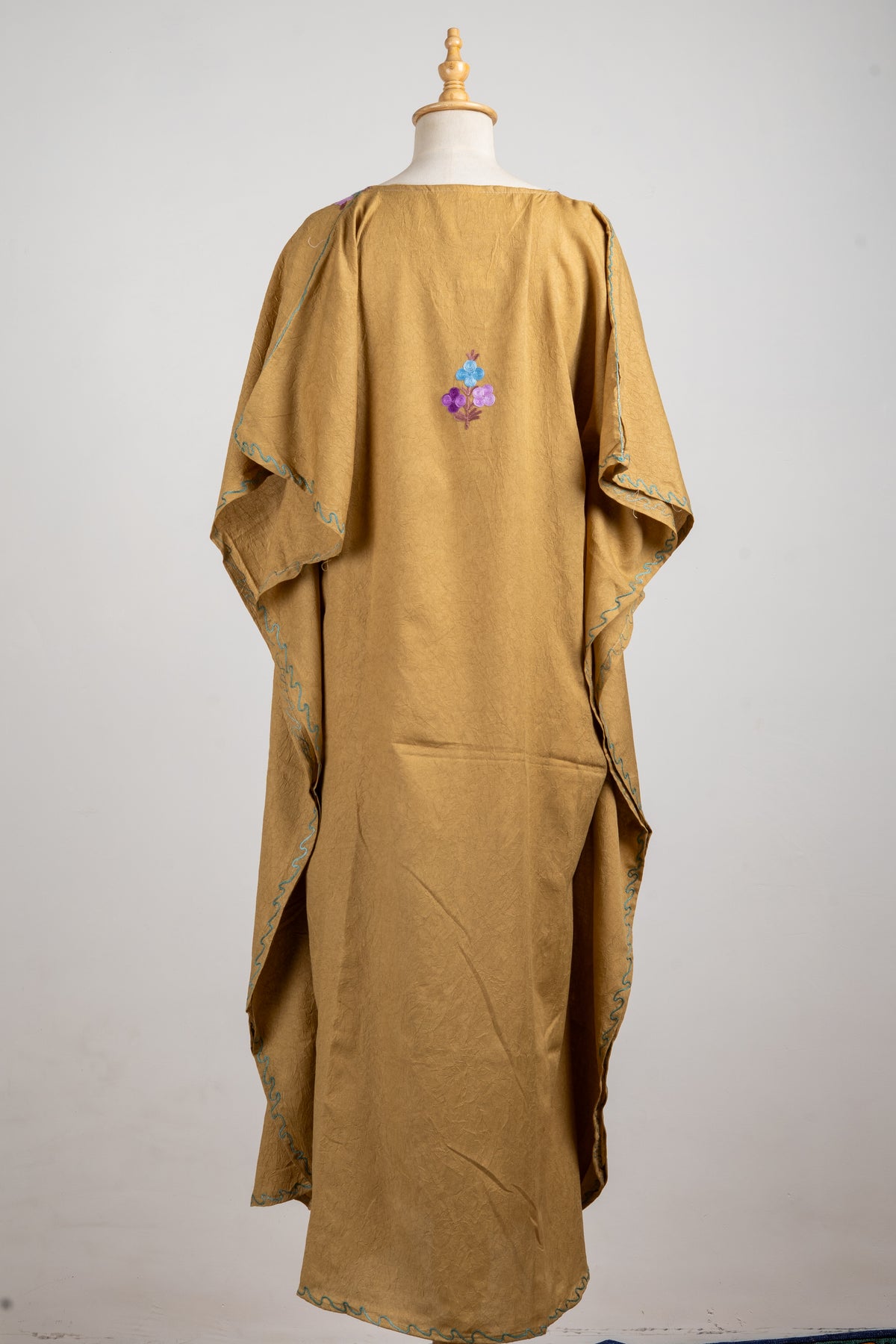 Full back view of the camel kaftan with a small embroidered flower sprig, loose sleeves and long plain body.