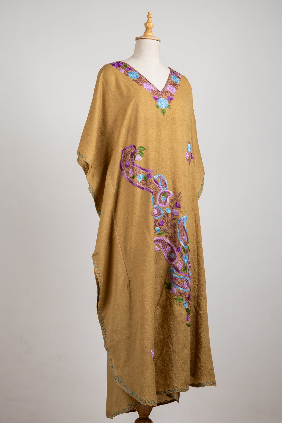 Angled full view of the camel kaftan showing a pastel floral neckline and a sweeping purple and blue paisley vine down the front.