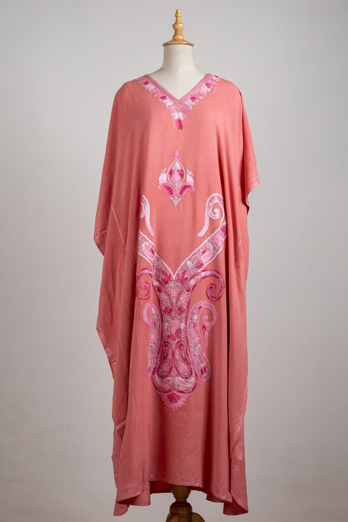 Full front view of a rose-pink kaftan on a mannequin, with a floral V-neck and large ornate pink paisley embroidery
