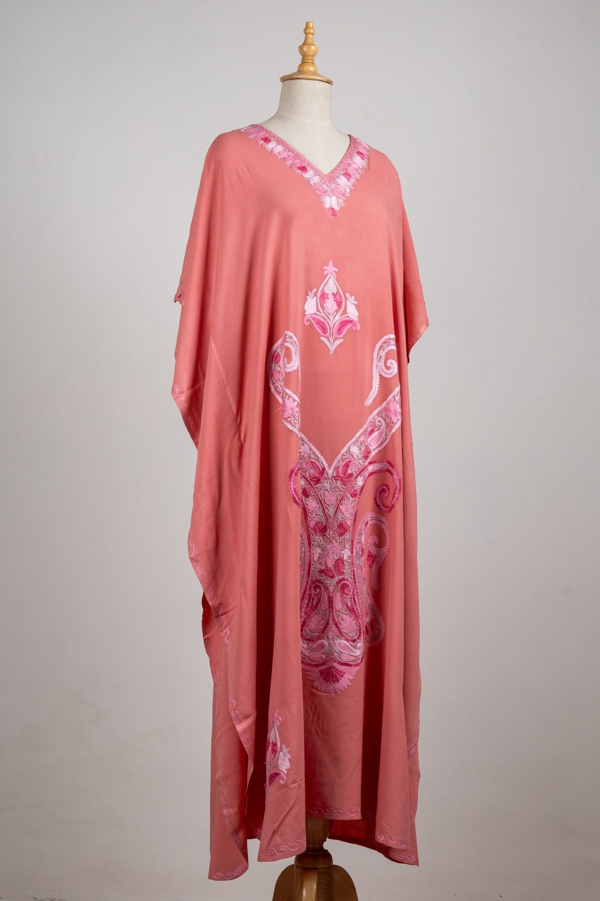 Angled full view of a rose-pink kaftan, with loose sleeves and a large symmetrical blush-and-fuchsia paisley design