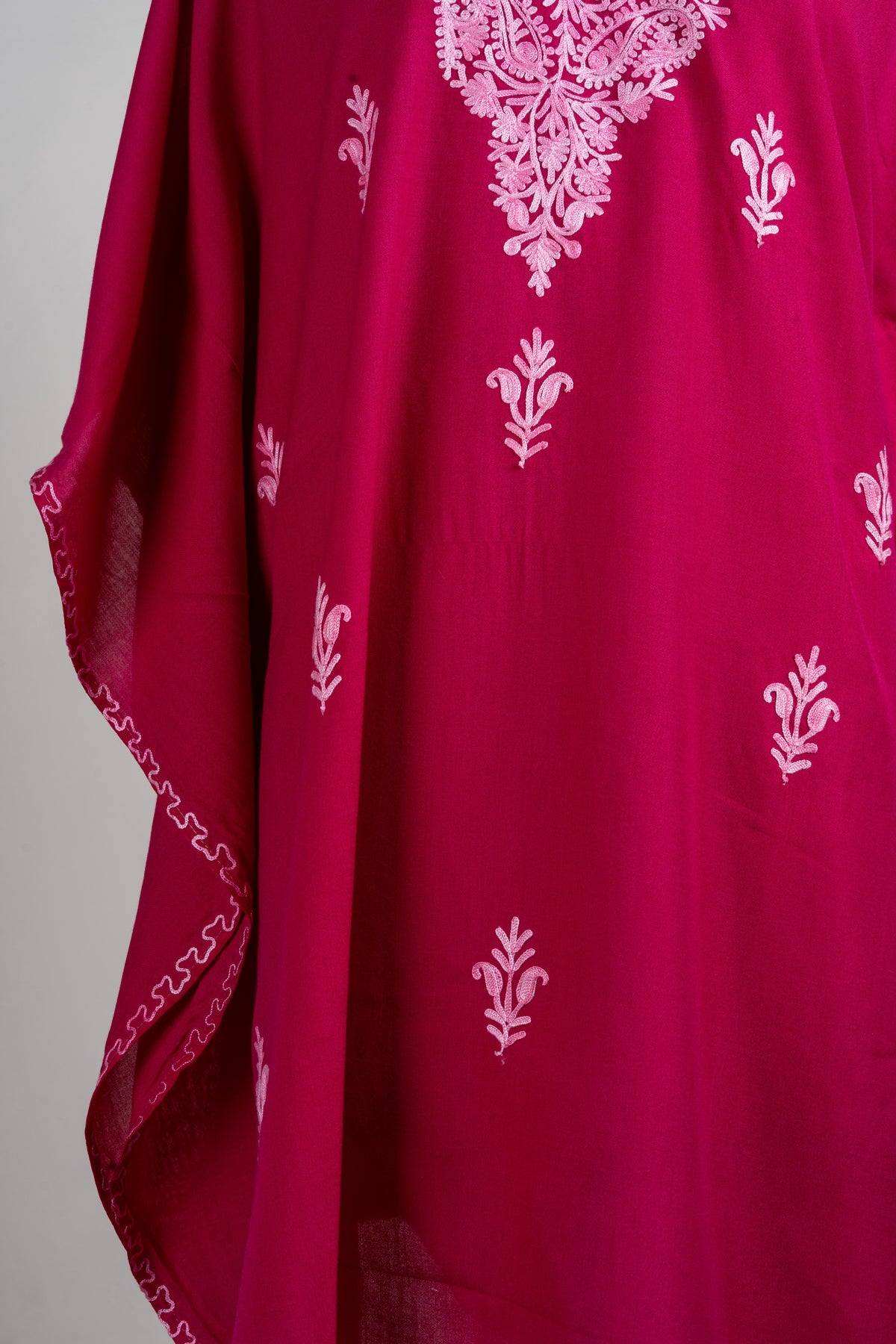 Detail of small pale pink floral sprigs across the ruby kaftan and wavy embroidery along the draped side edge