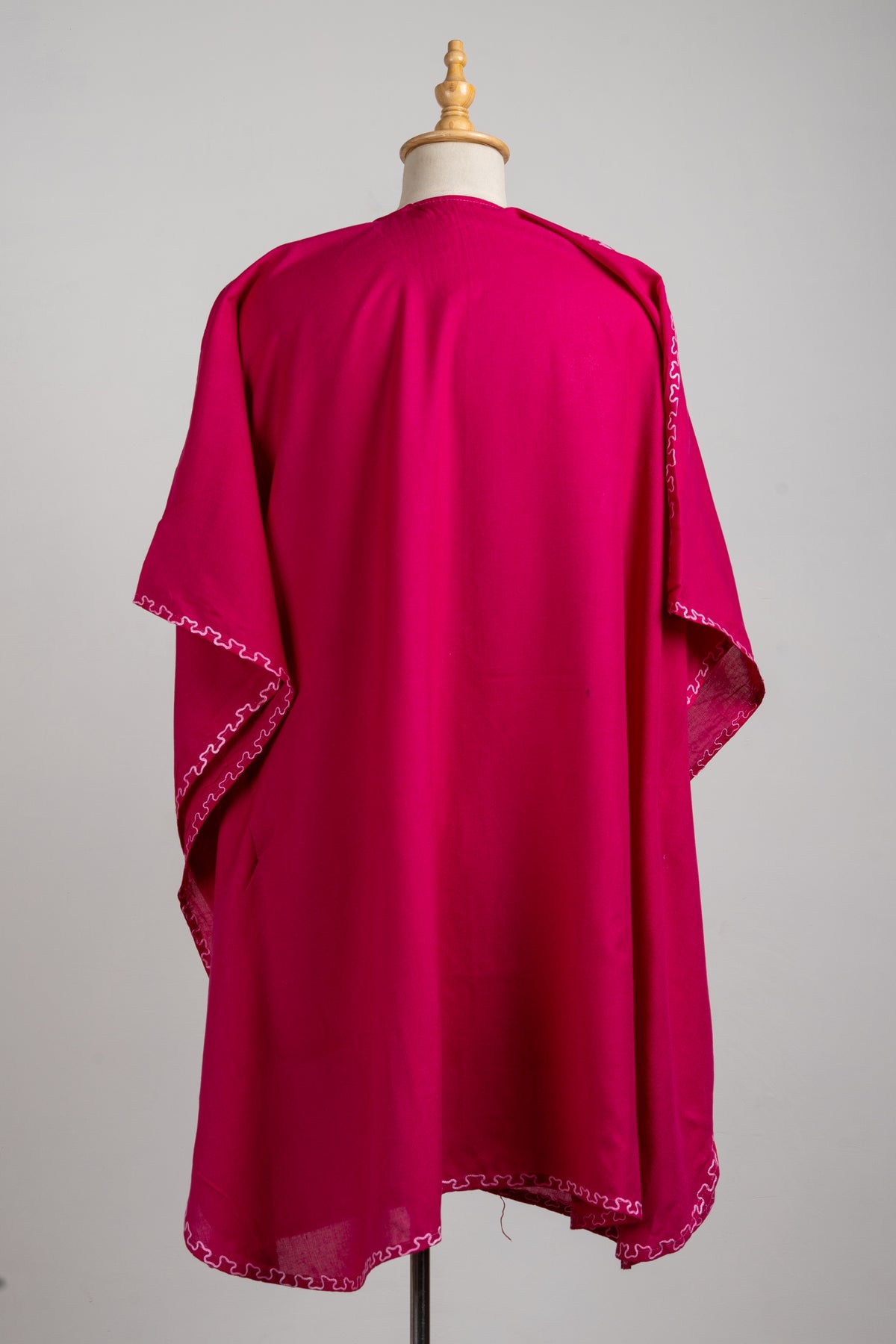 Back view of the plain ruby pink kaftan with pale pink wavy stitching along the sleeve edges and hem