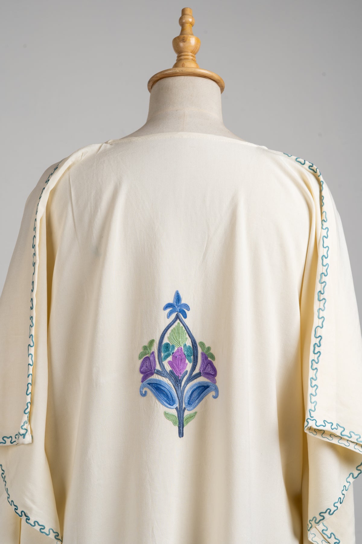 Upper back detail of the ivory kaftan showing a blue and purple flower motif beneath the plain round neckline.